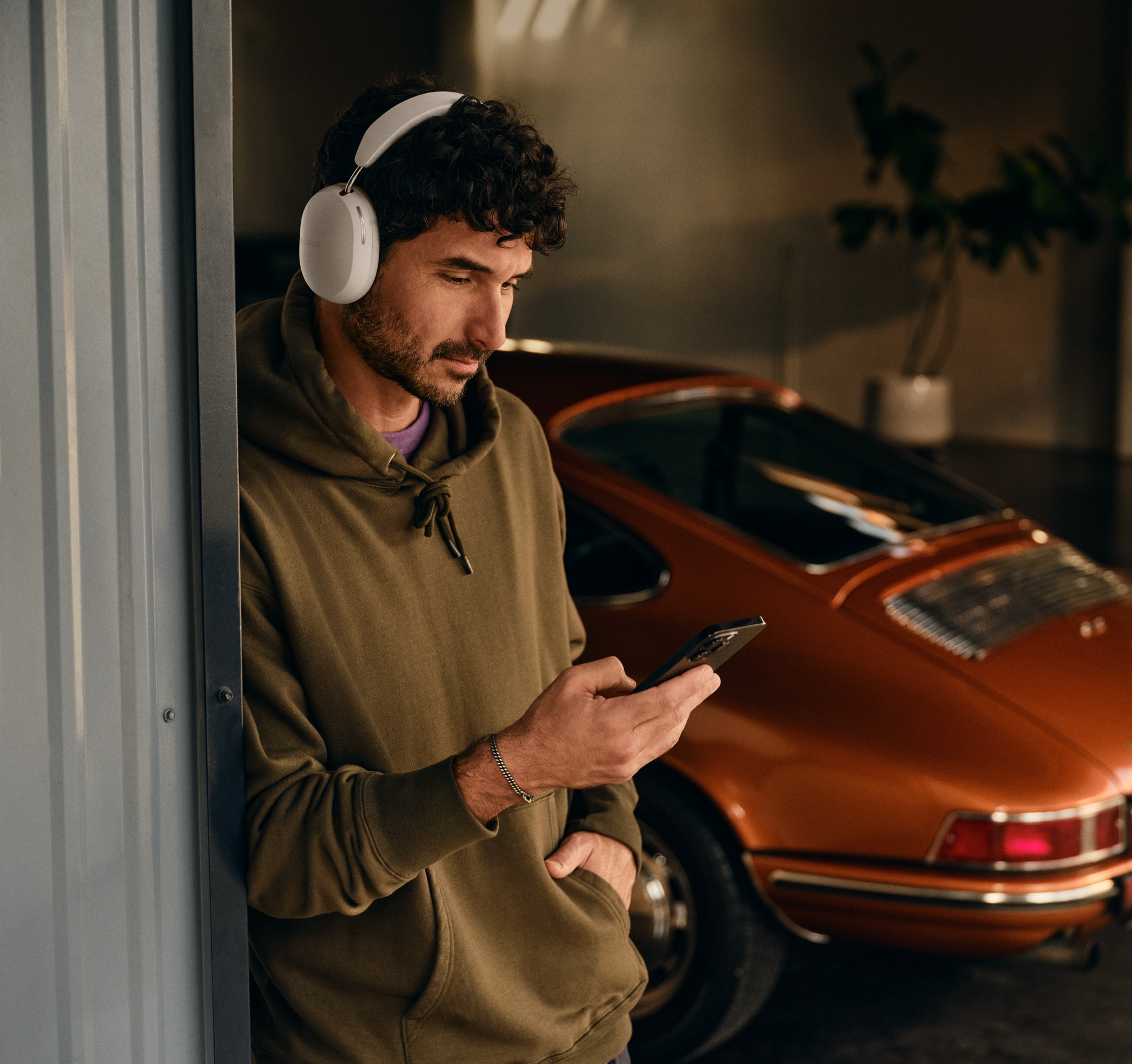 Person wearing white Sonos Ace and using his phone next to a car