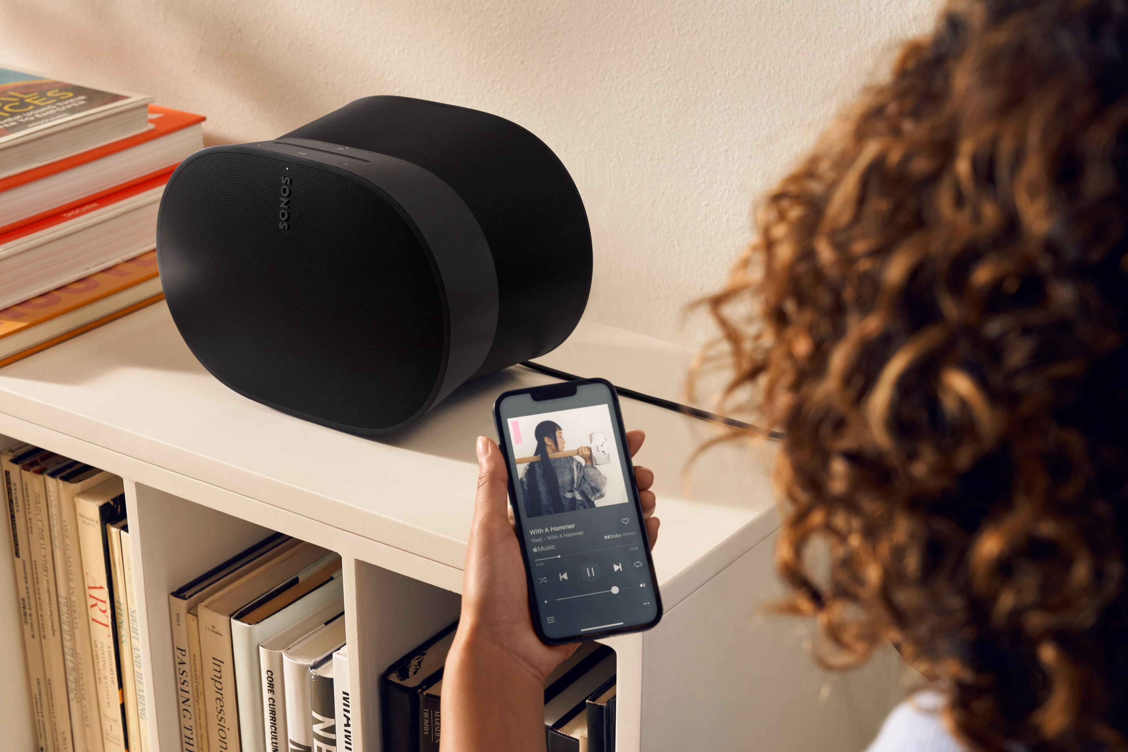 Woman using her phone to control a black Era 300 on a bookshelf