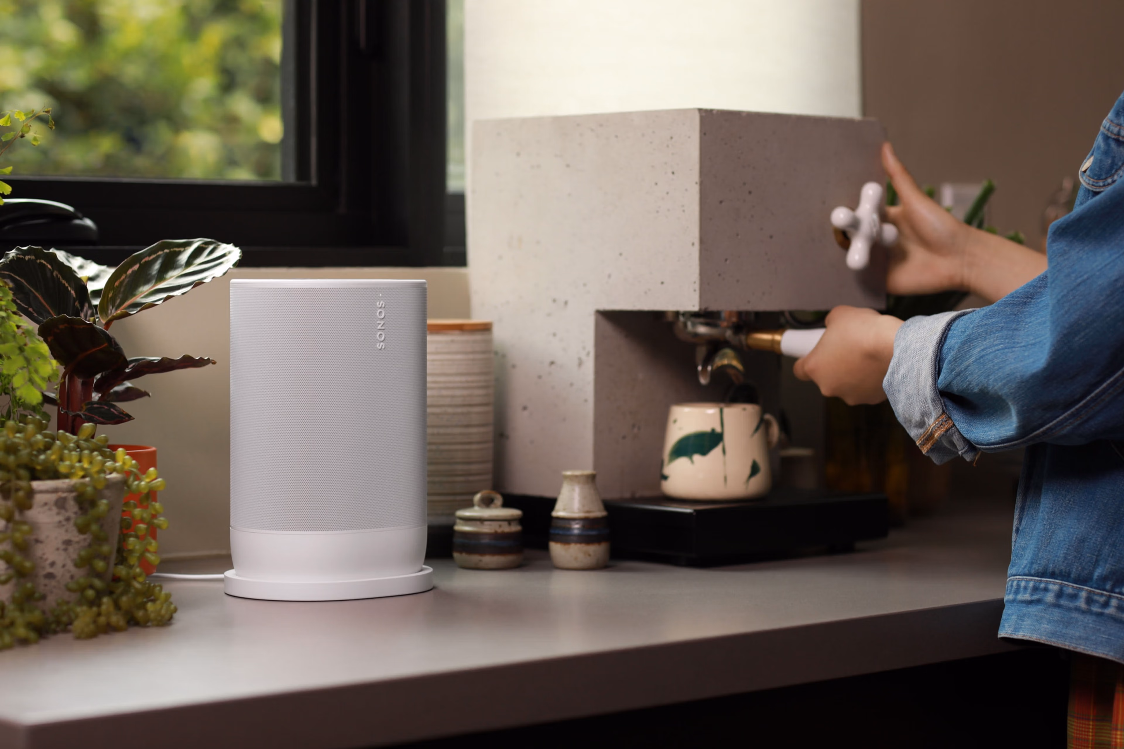 Kuva naisesta valmistamassa espressoa keittiön työtason ääressä valkoisen Sonos Move 2:n vieressä