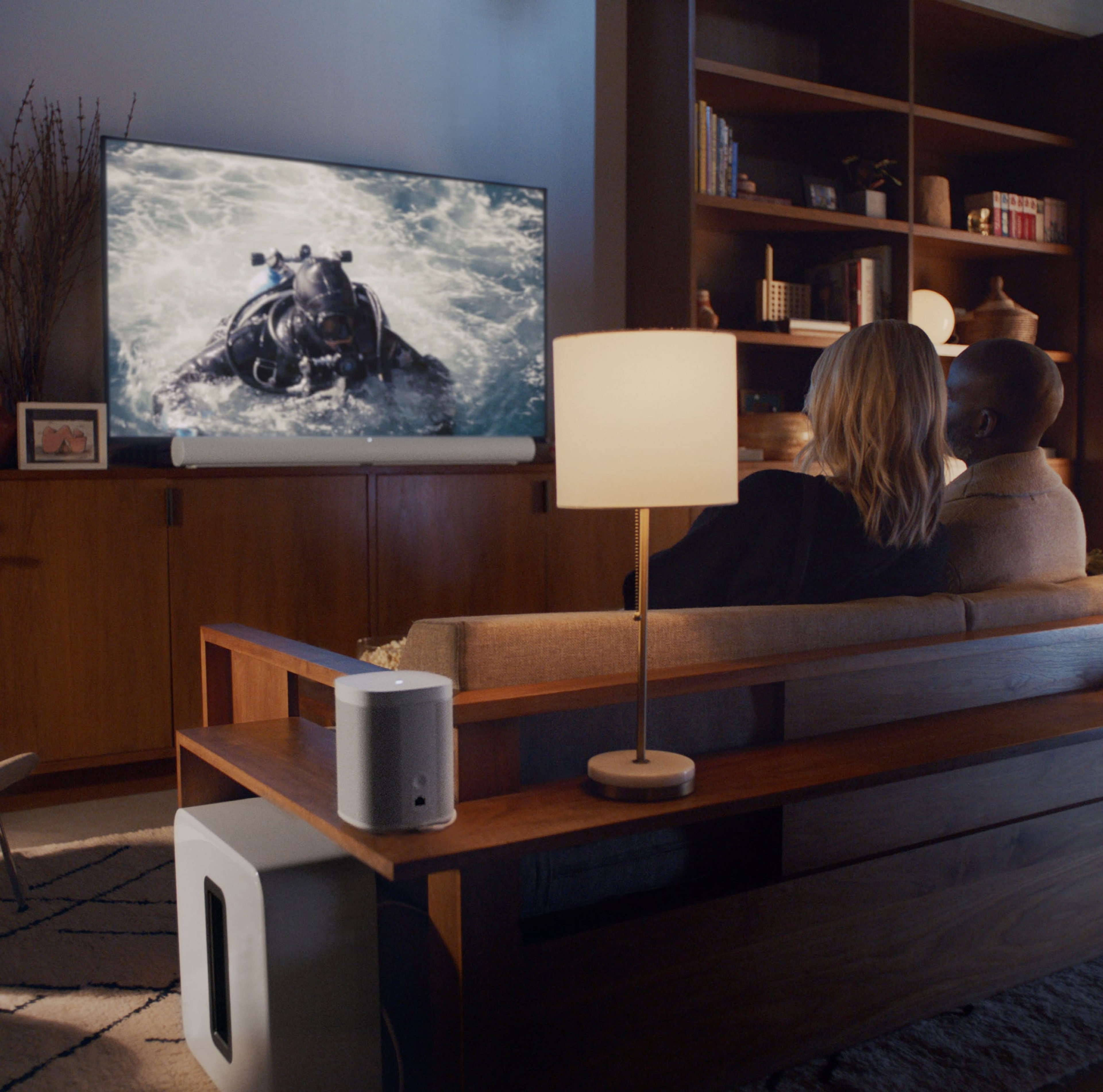 Una pareja mira TV en un sistema de teatro en casa con Sonos Arc en blanco