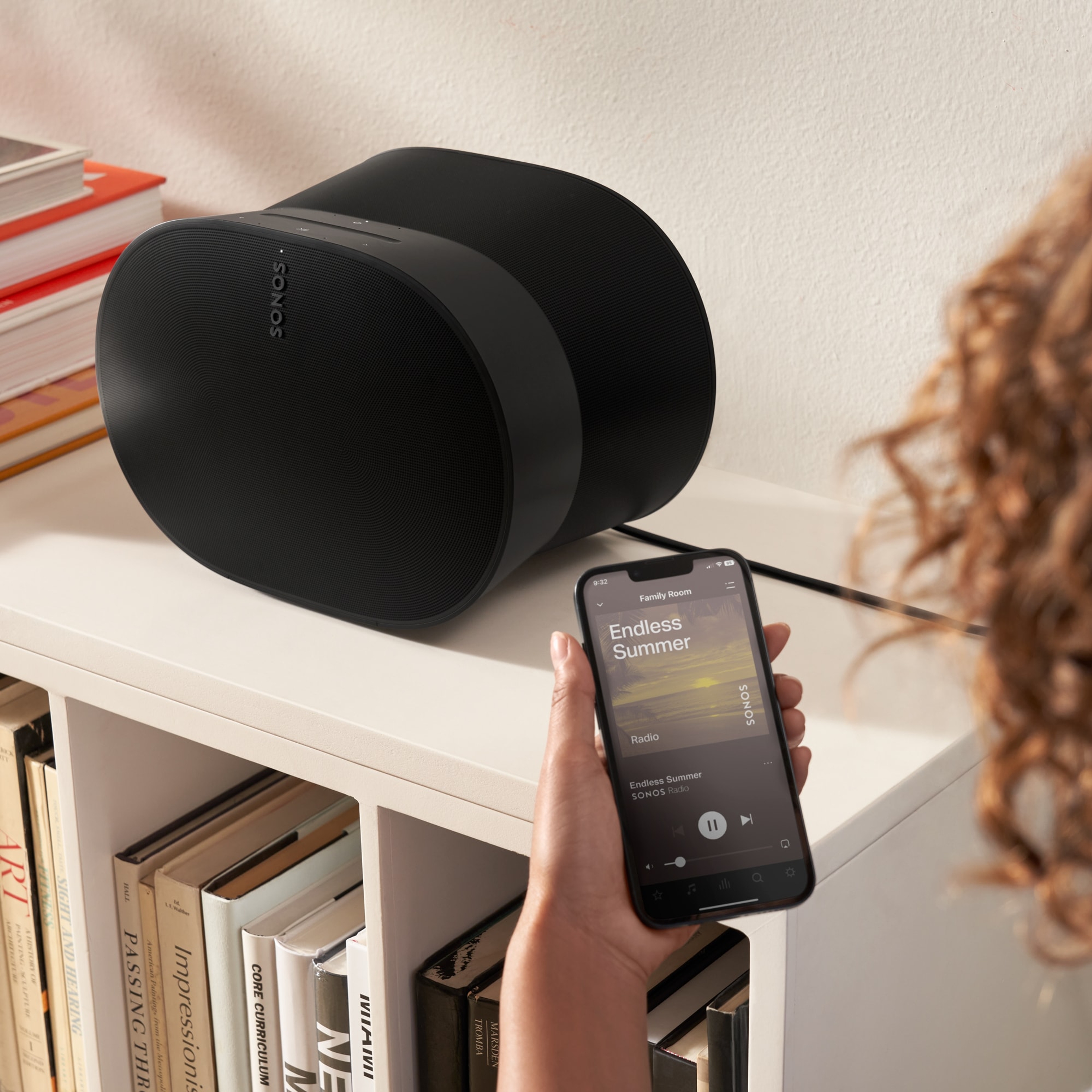 Woman using her phone to control a black Era 300 on a bookshelf